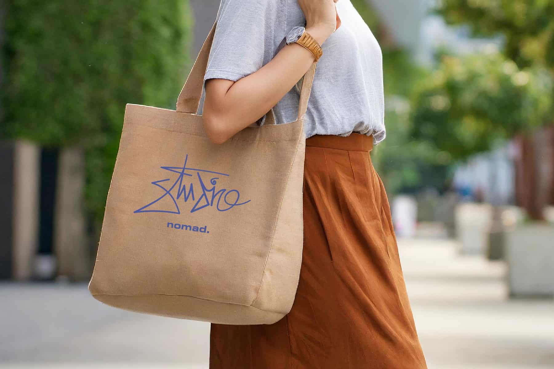 Studio Nomad logo on a tote bag someone is holding outside.