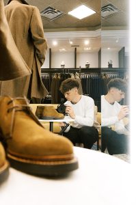 Geoffrey Faber taking a photo in a large mirror that reflects himself and scene inside a luxury men's clothing store