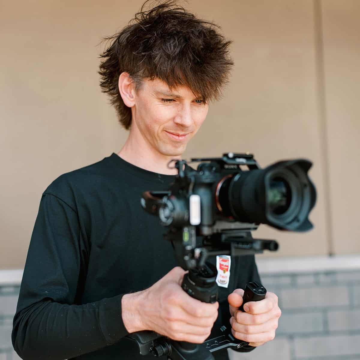A videographer looking at the back of his camera while filming using a gimble set up.